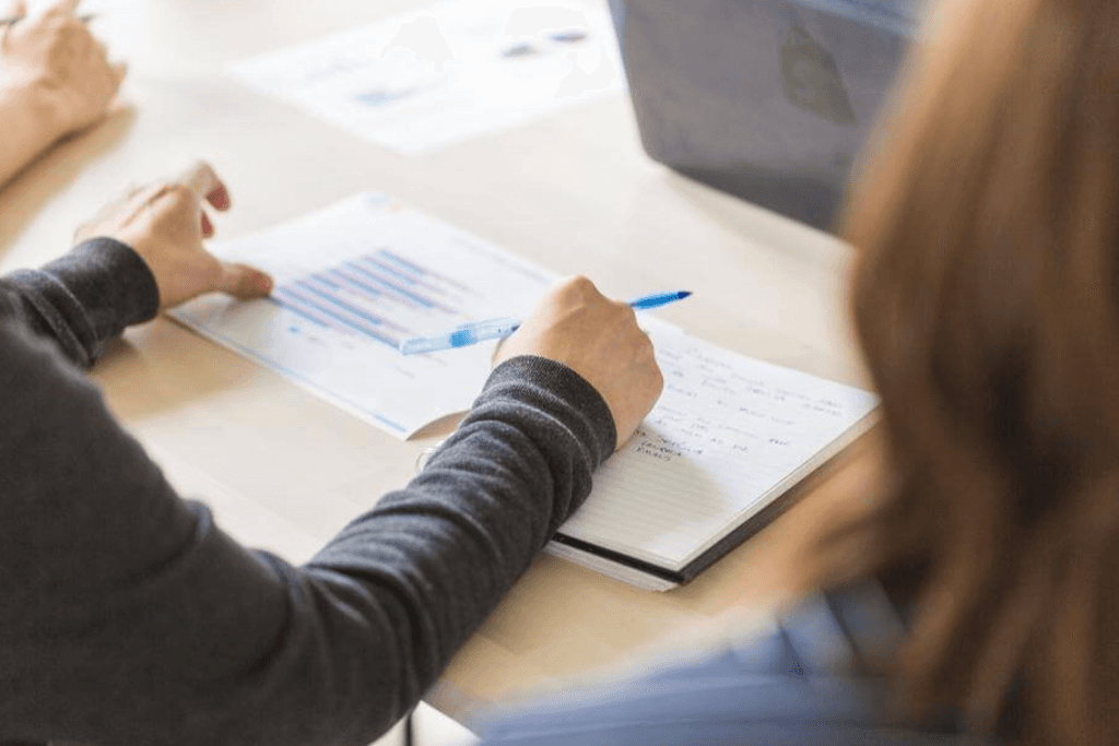 Two people reviewing a printed bar chart and handwritten notes at a desk