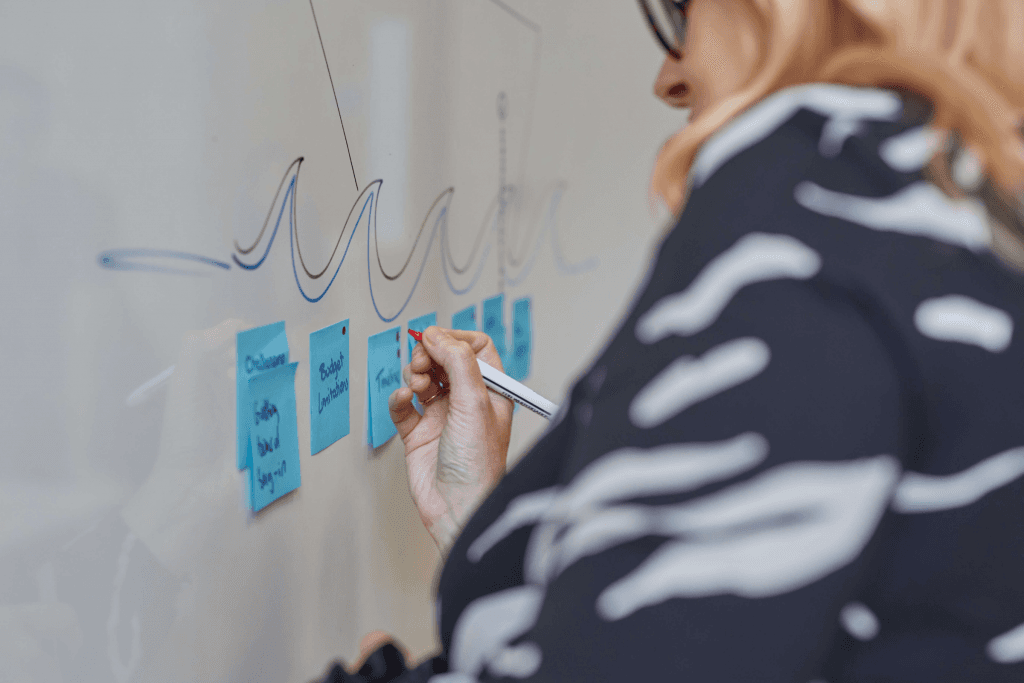 A facilitator adding blue sticky notes labelled challenges, budget limitations and timelines beneath the waves of the sailboat drawing
